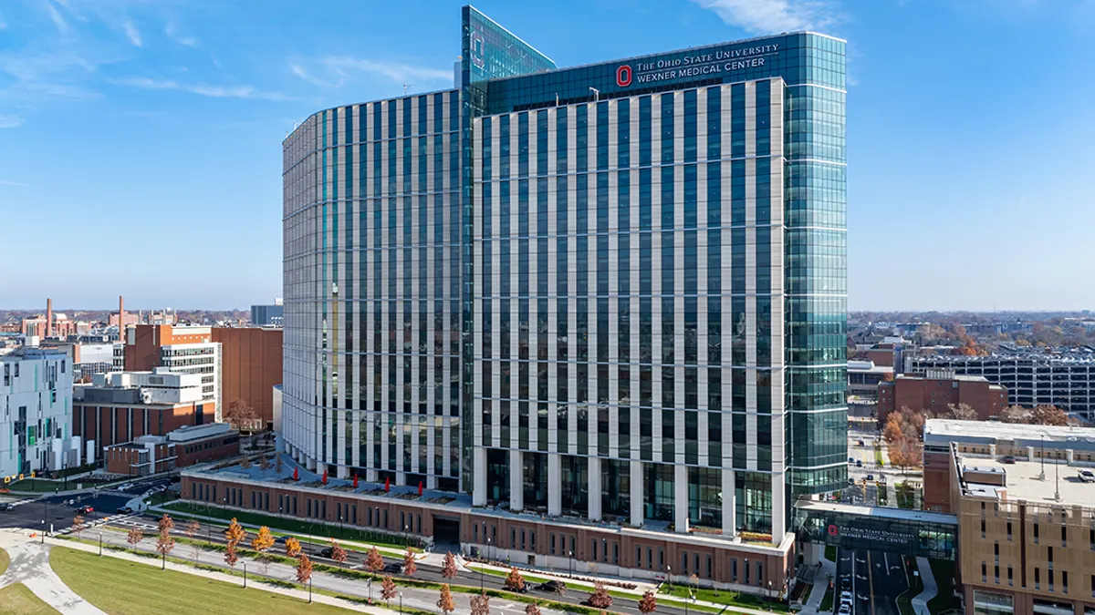 A photograph of a massive, glass-covered building that rises in the middle of green space on a bright day.
