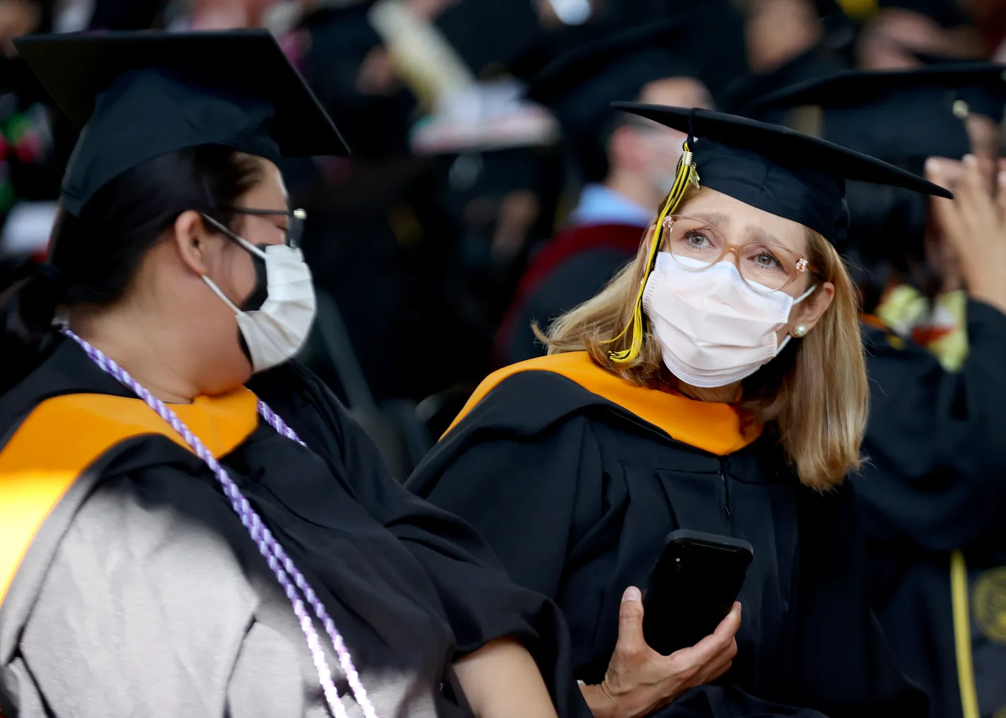 Two people dressed in graduation caps and gowns wear masks at their commencement.