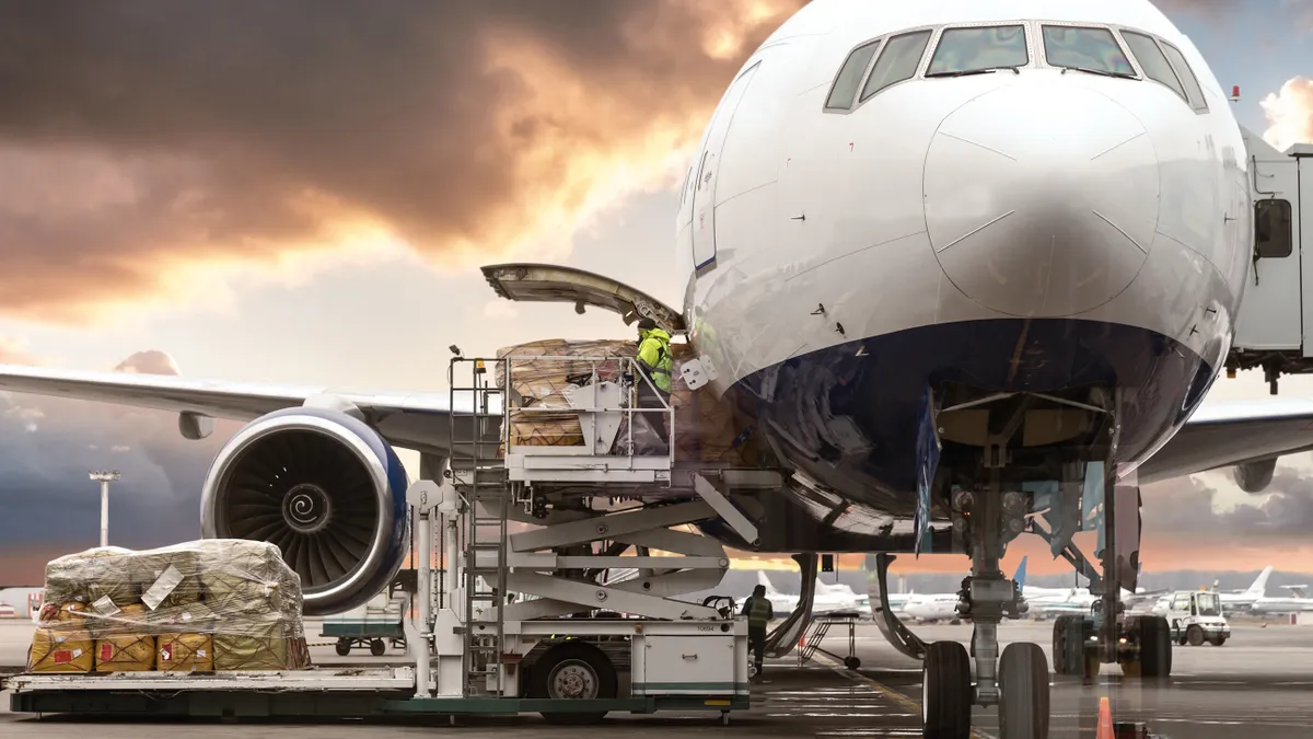 Cargo is being loaded into the belly of a passenger aircraft, with other airplanes in the background