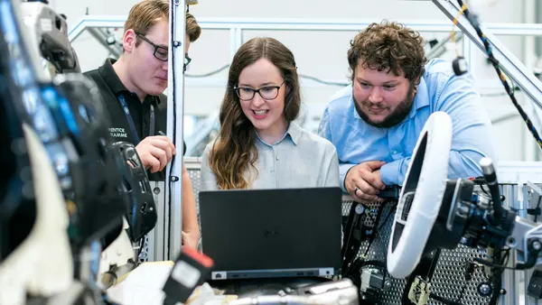 Three workers engage with a laptop in a factory, highlighting teamwork in a manufacturing environment.