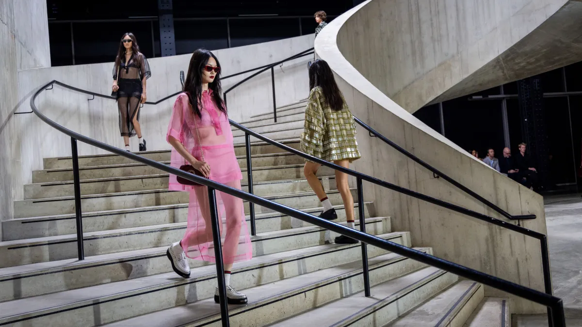 Models in sheer clothing and short skirts walk down a curved staircase.