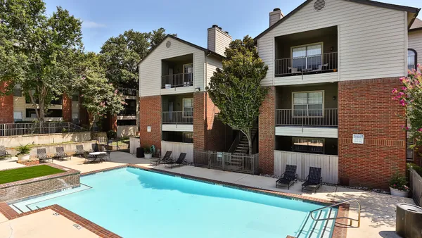 Tan and brick apartment building with a pool in the foreground.