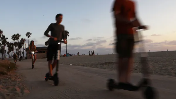 Several people riding electric scooters along a path silhouetted against an evening sky.