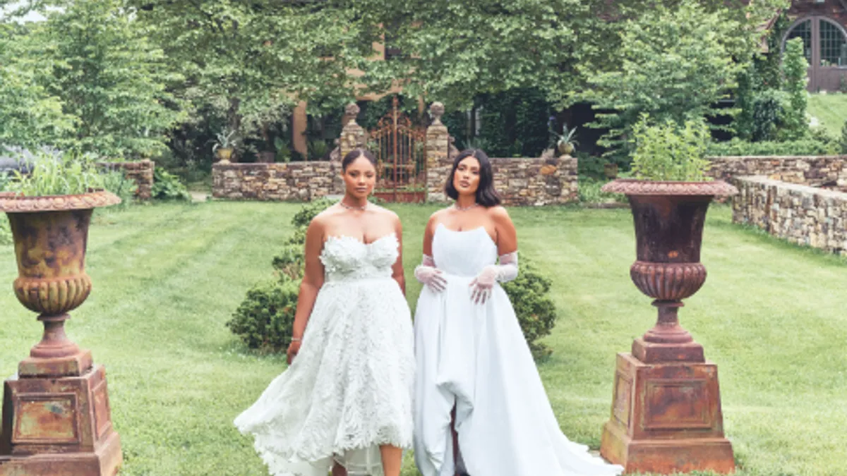 Two brides stand outside wearing white wedding dresses.