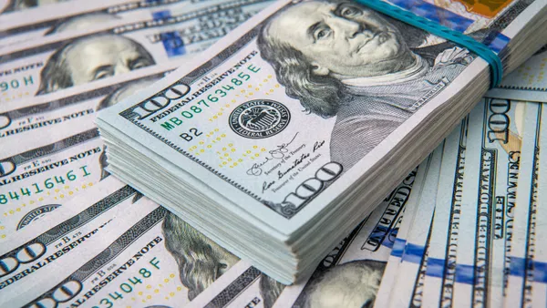 A close-up picture of a stack of one hundred dollar bills on top of fanned out one hundred dollar bills.