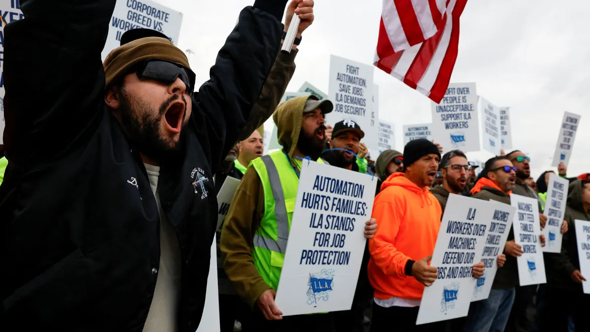 A group of people in bright gear, sunglasses and hats hold signs. They are yelling and speaking in the photo.