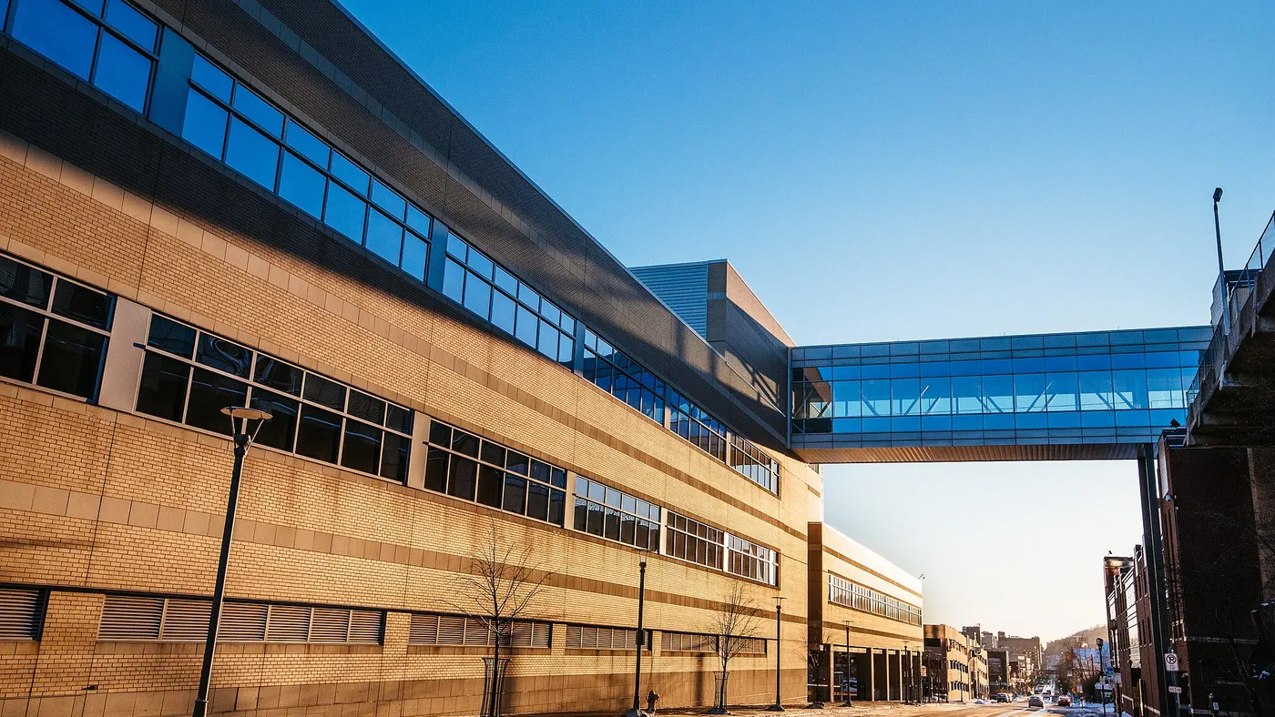 A hospital skyway over a street between two buildings appears against a clear blue sky on a snowy day.