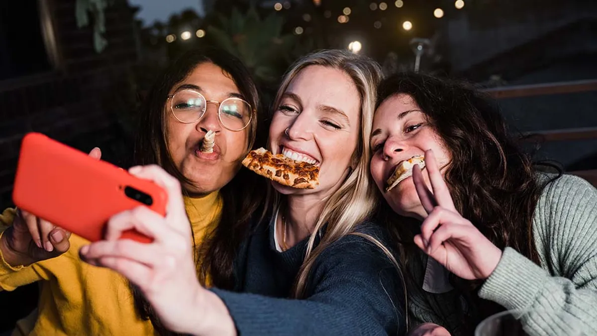 Girls having fun together outdoors in restaurant while taking selfie with smartphone