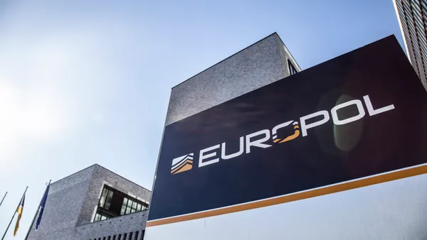 A sign reading "EUROPOL" sits outside a large gray building, with two flags hanging from flagpoles at the left edge of the photo