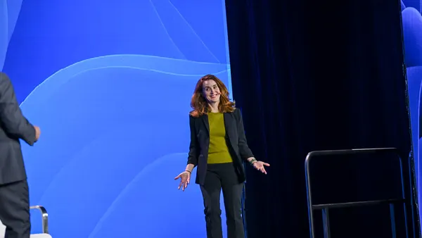 a woman stands on a keynote stage being introduced