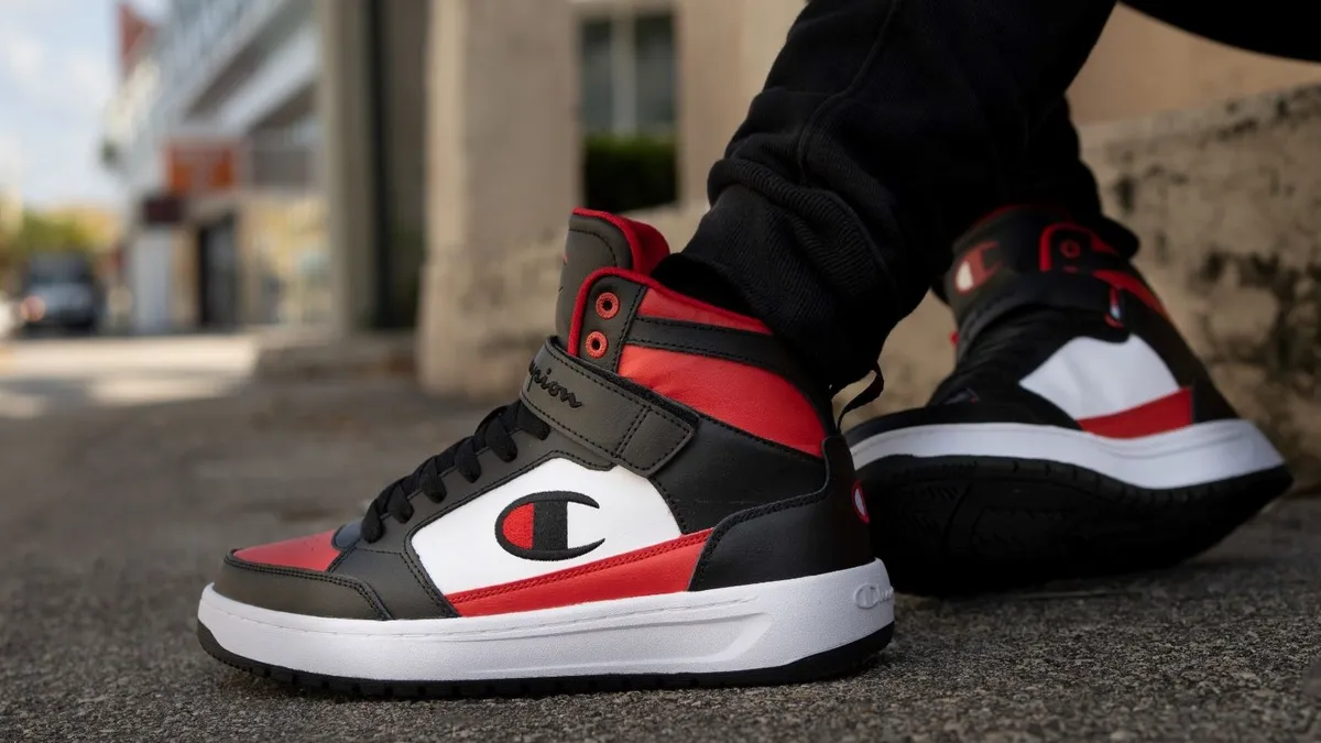 A closeup of the feet of a person wear a pair of Champion brand sneakers in a red, black and white colorway.