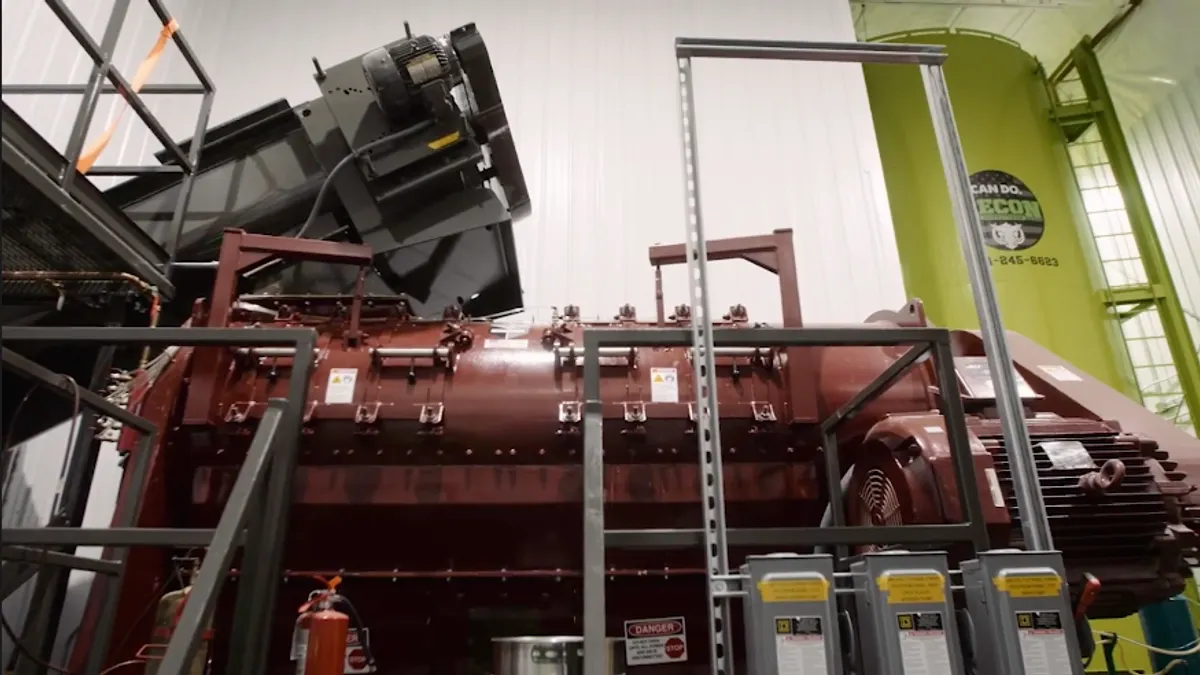 An industrial machine inside a building has a loading ramp and several turning components.