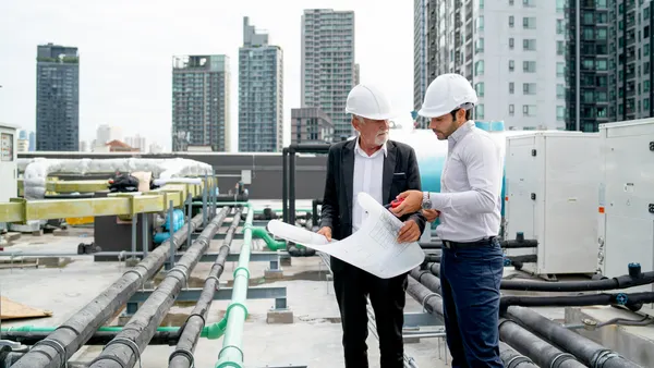 An engineer and technician on a city rooftop discussing blueprints.