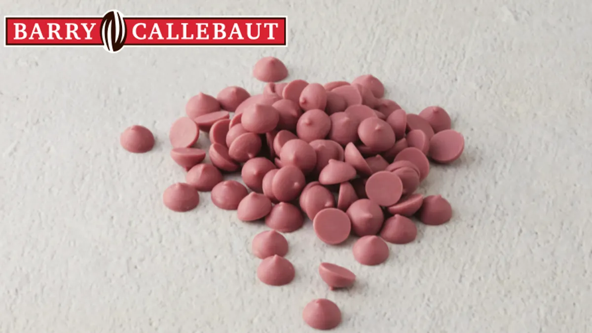 A small pile of dark pink ruby chocolate chips on a white textured surface with the Barry Callebaut logo in the upper left corner