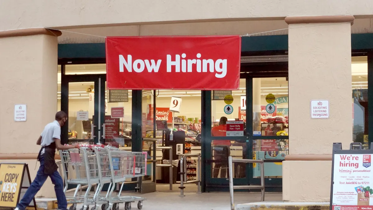 A Now Hiring sign hangs near the entrance to a Winn-Dixie Supermarket on September 21, 2021 in Hallandale, Florida.