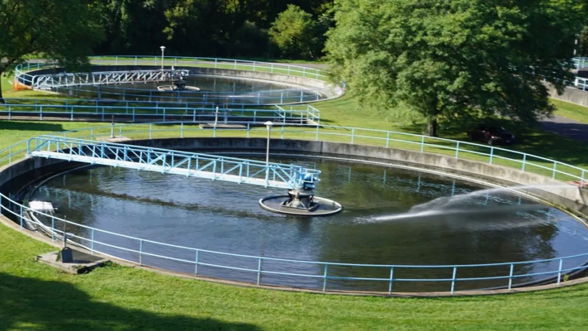 A pair of circular engineered outdoor ponds with a pipe spraying into each pool and a catwalk to each pool's center.