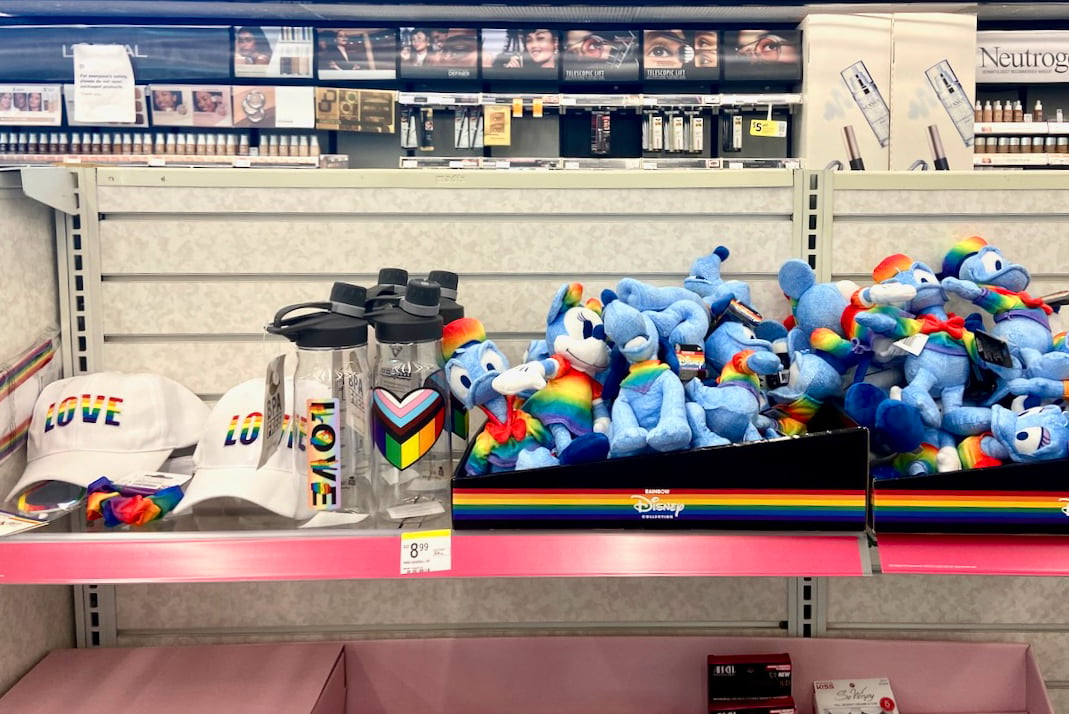 A small shelf of hats, small stuffed animals and other objects decorated with rainbows for Pride.