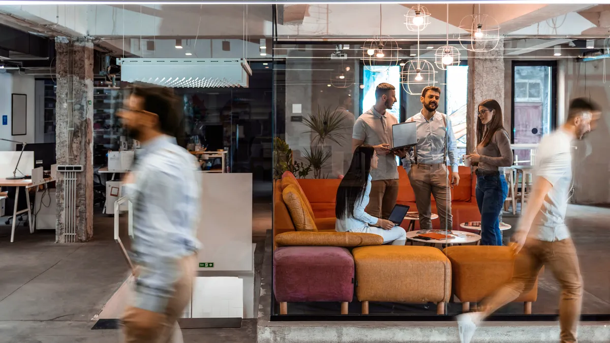 Employees work in an office shared space while others walk by.