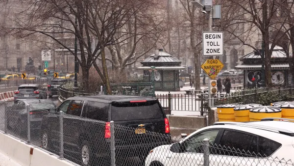 A line of vehicles passing a sign that reads "Begin toll zone."