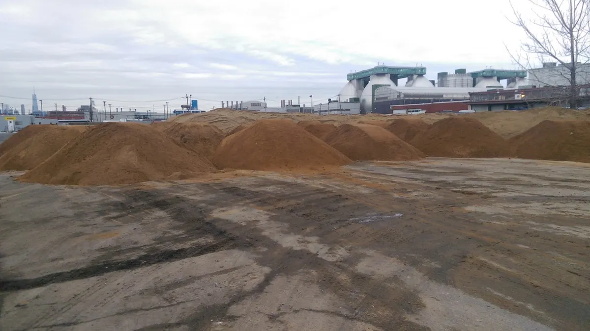 Yellow earth mover moving a pile of soil on a pier jutting out from a beach.