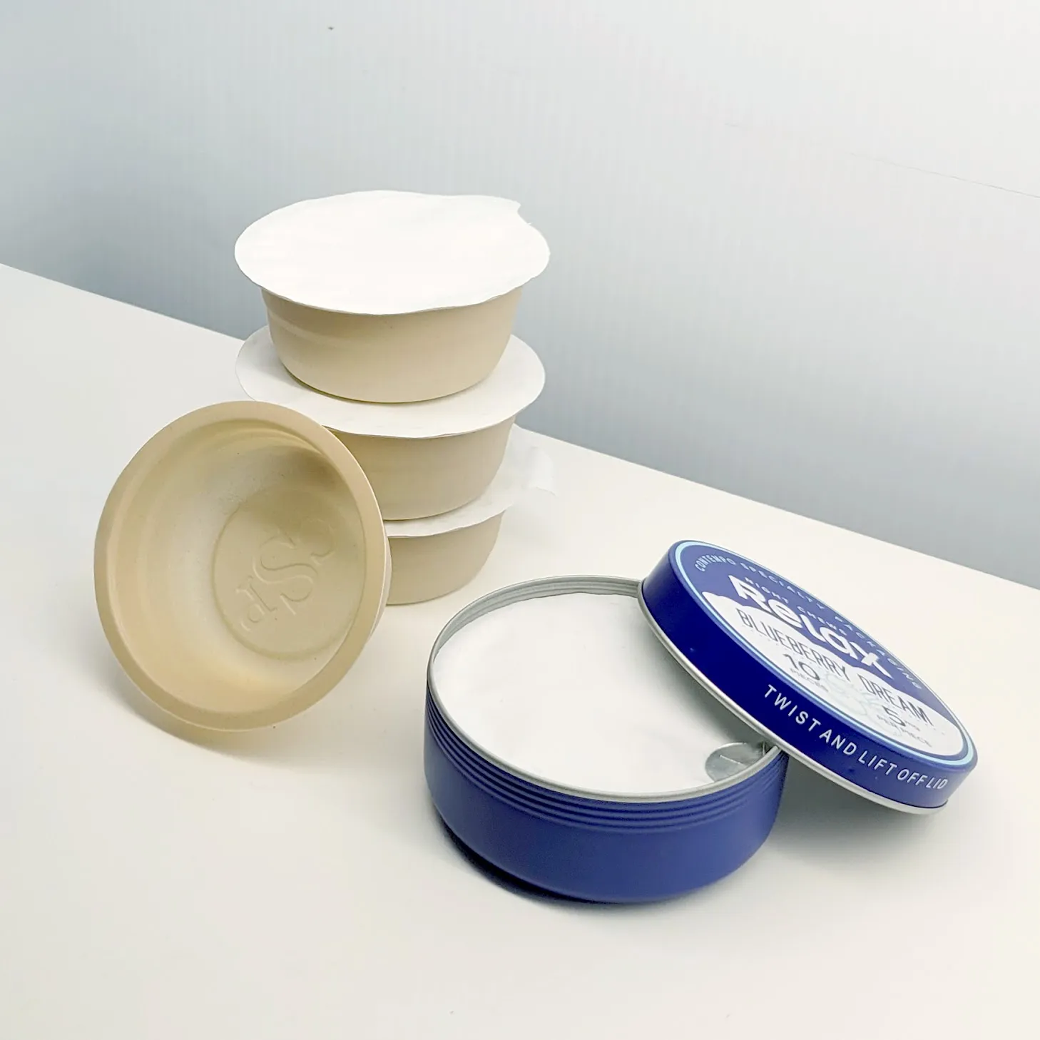 A stack of beige-colored packaging pods next to a blue metal tin.