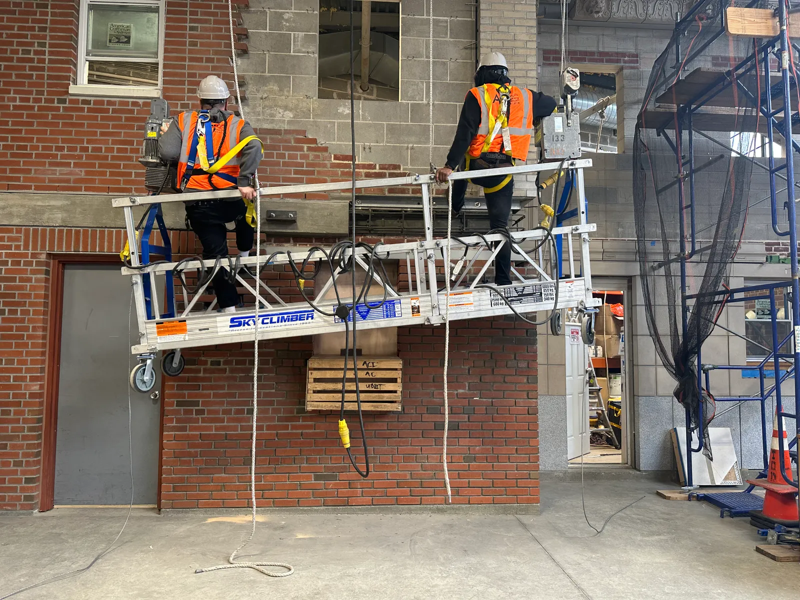 Two construction workers on a lift within a warehouse placing bricks in a facade.