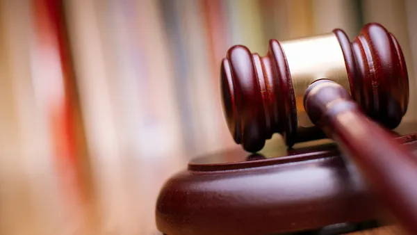 Close up shiny wooden law gavel in dark brown color on top of a wooden table in an office.