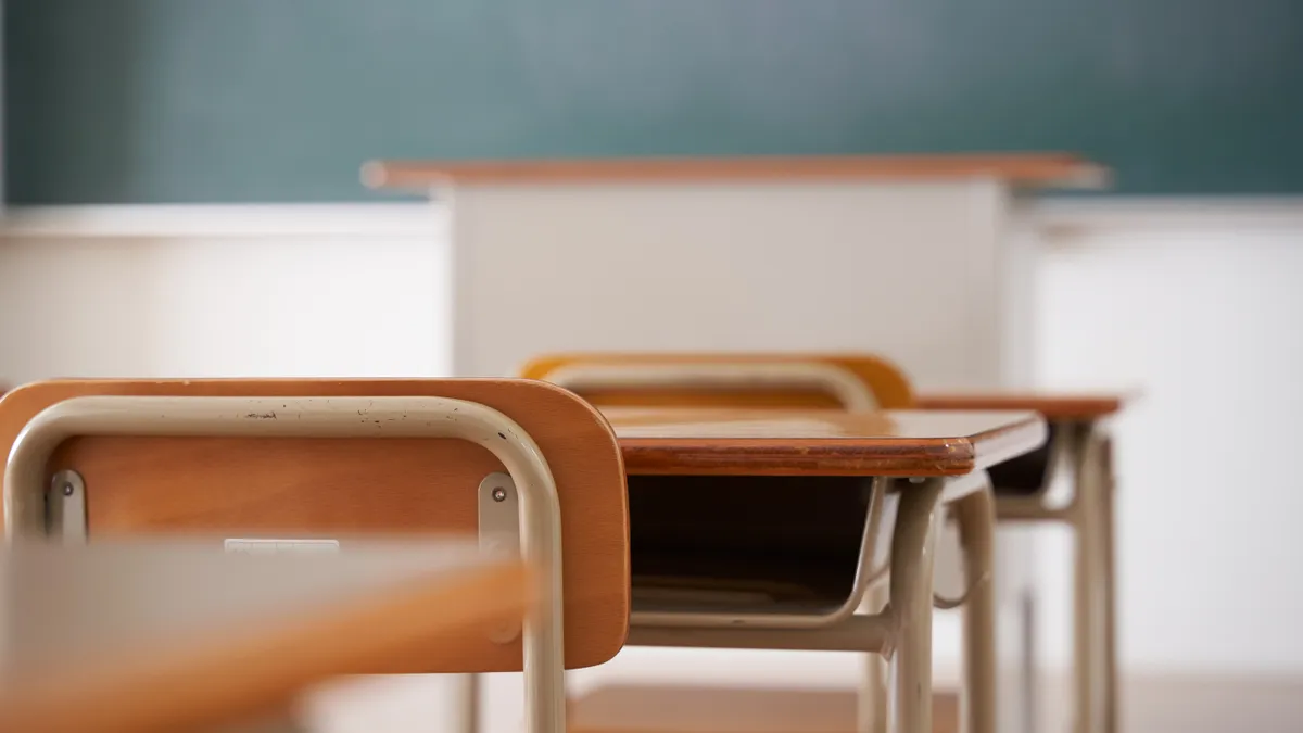 A photo of a classroom shows an upclose image of a student desk with other desks out of focus.