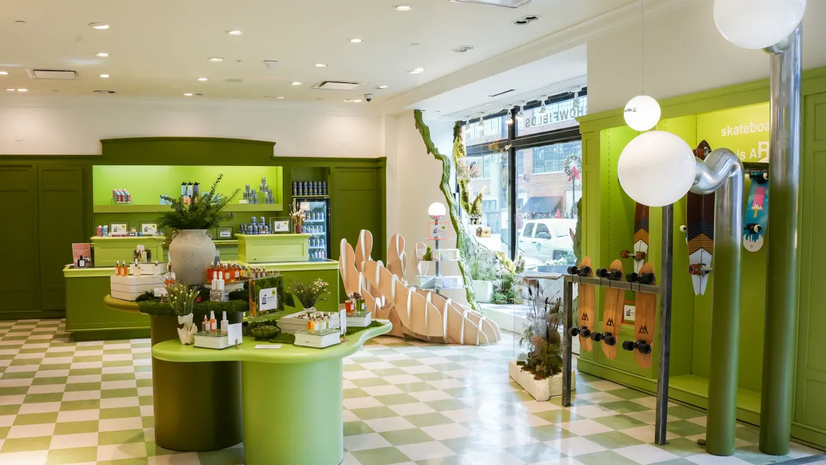 Interior of a Showfields store. Shelves are painted green and feature a variety of products like skateboards and beauty items. The floor is green and white checks.