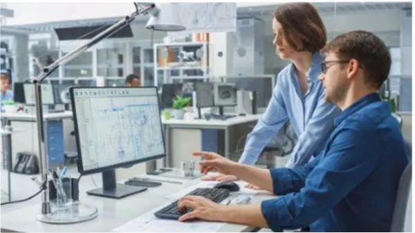 Engineer talking with a project manager while working on a desktop computer
