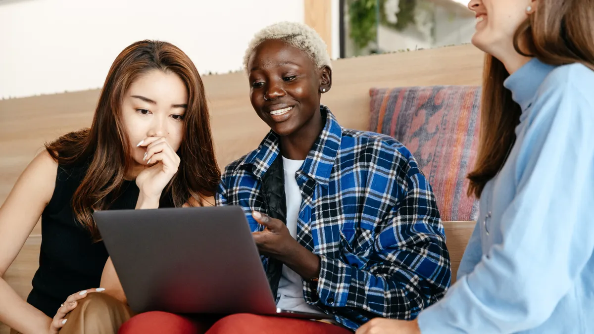 Three people sit side-by-side looking at a laptop