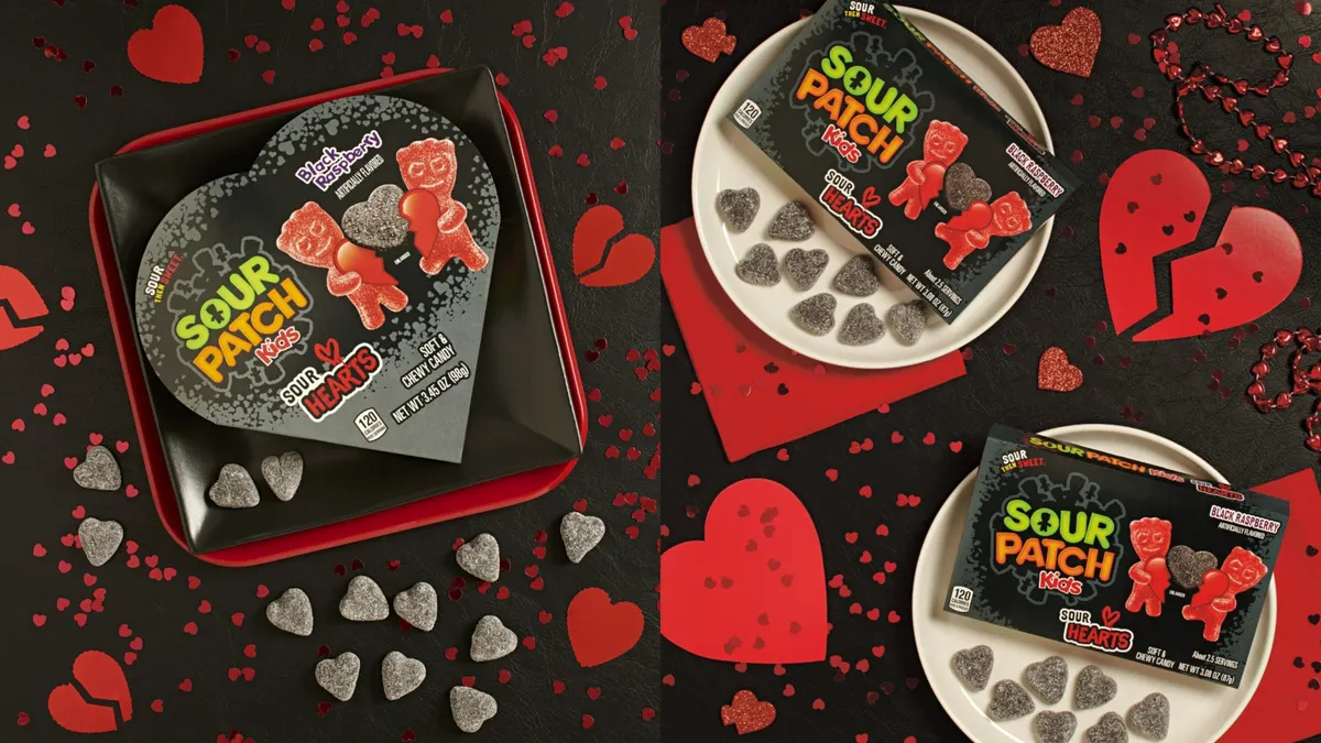 Three black heart-shaped boxes of Sour Patch Kids Sour Hearts candy, with black candy hearts around them. The candy and boxes are on a black background with red broken hearts.