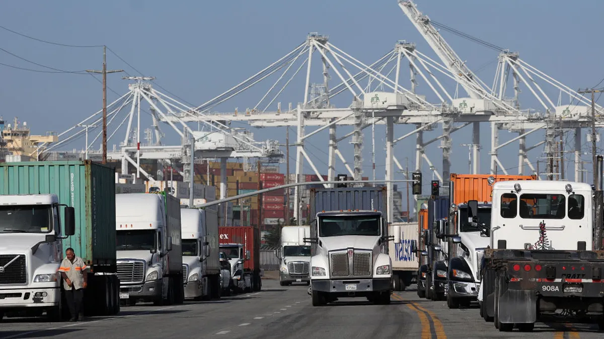 Trucks carrying shipping containers drive through an ocean port.