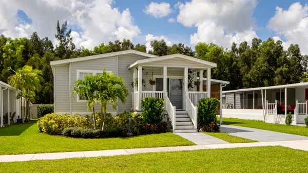 A small gray house with a green lawn under a blue sky with clouds.