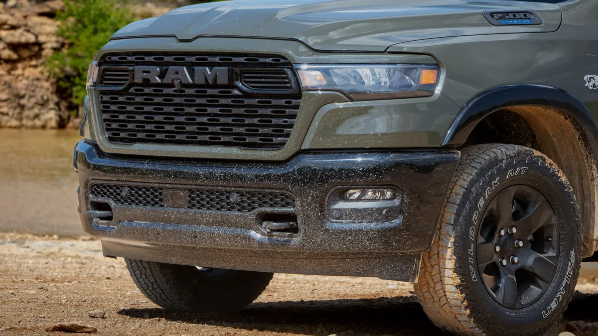 The front grill of a 2026 Ram 1500 BackCountry pickup parked outdoors on a dirt surface with mud on the tires.
