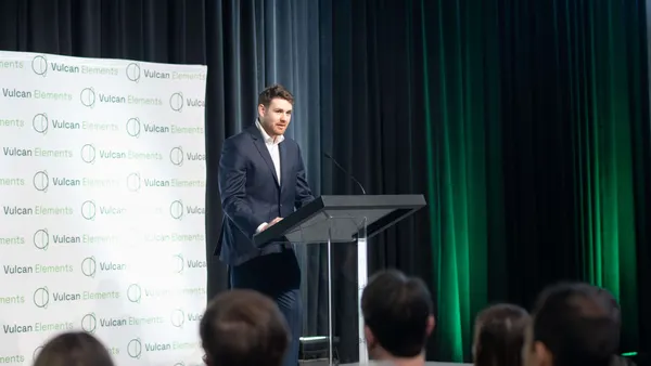 A person in a blue suit standing behind a podium and giving a speech.