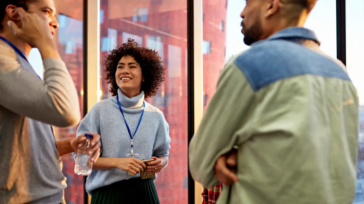 Waist-up view of smiling Latinx person standing and talking with Black and multiracial colleagues in late afternoon sunlight