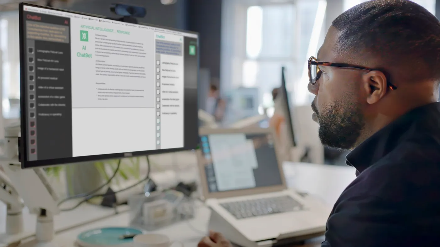 A person's face looking into a computer screen in an open plan working office. Type is being added to the screen by an Artificial intelligence, AI, chatbot.