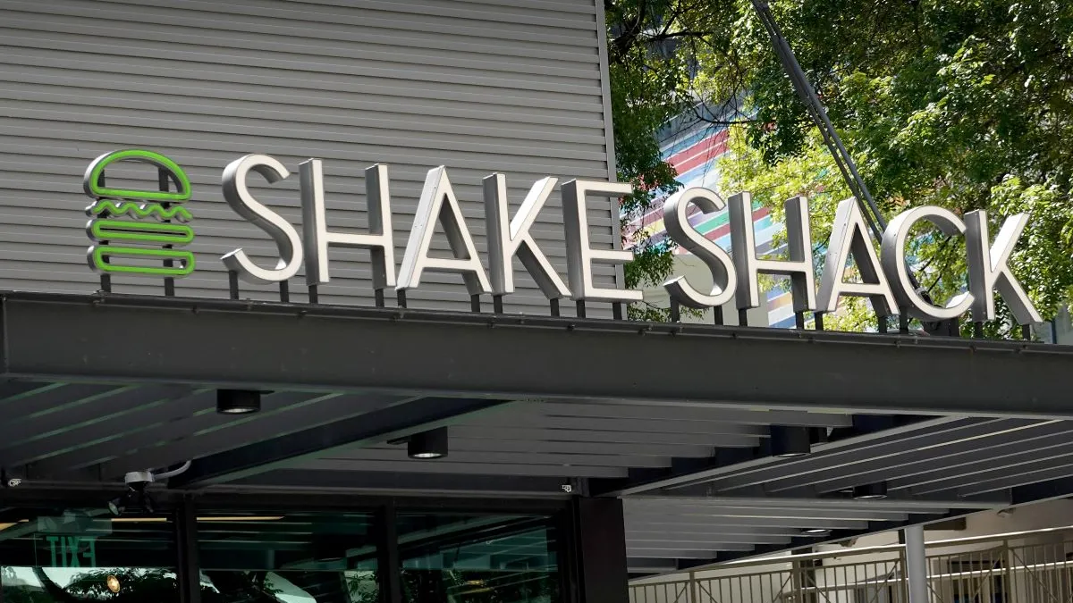 An image of a store sign that says Shake Shack. To the left is a green neon sign of a burger