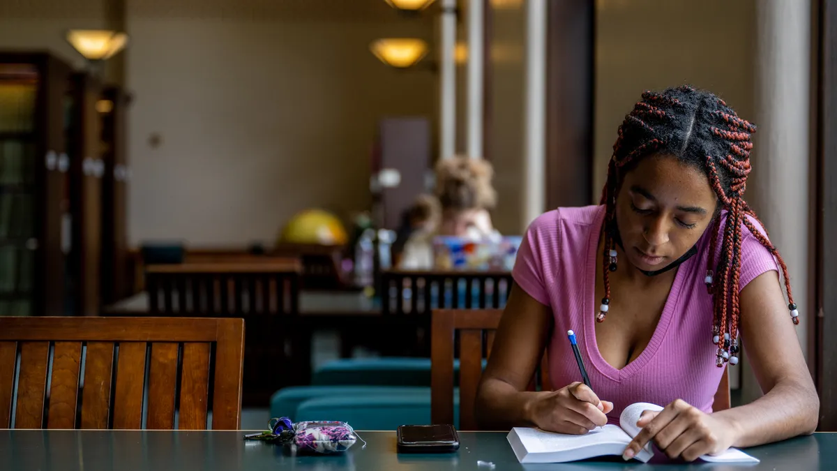 A person sits at a table holding a book and pencil.