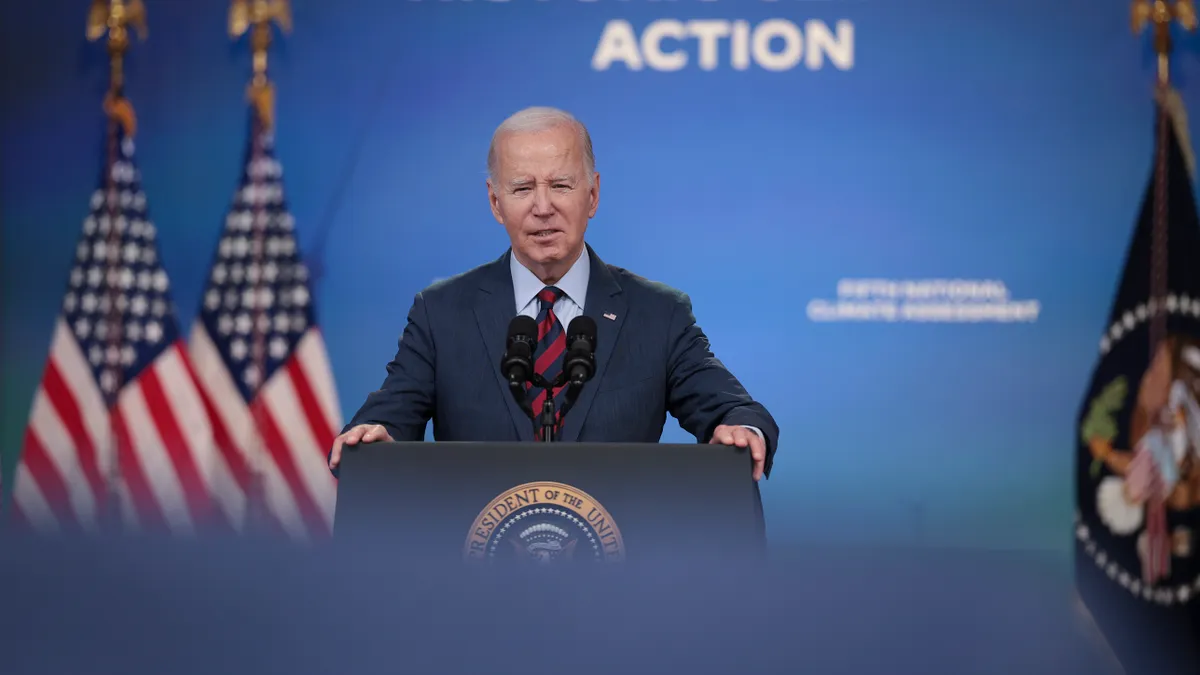 U.S. President Joe Biden stands at a podium at the White House with American flags behind him and a blue backdrop that says Historic Climate Action.