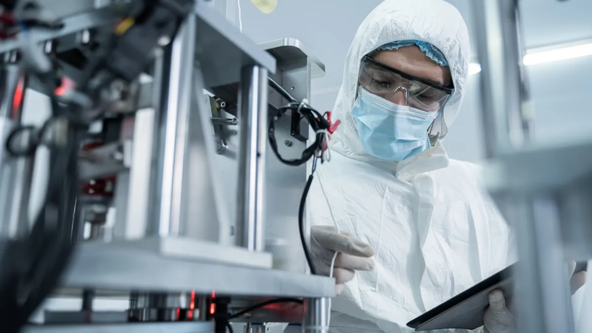 A medical professional in a white suit and mask working on a tablet