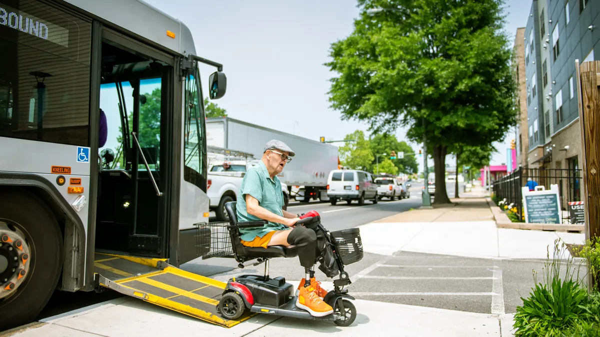 An older adult in a wheelchair exits a bus on a ramp.