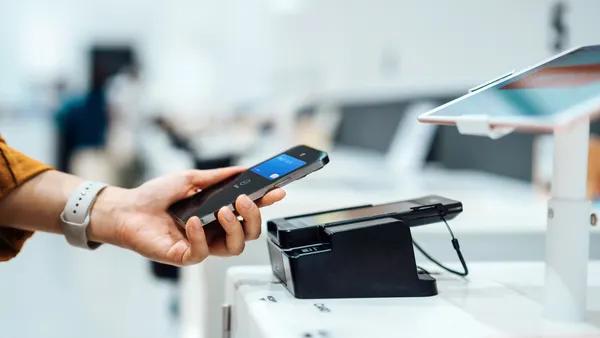 Close-up shot of a female hand holding smartphone near to a credit card machine, making contactless payment to pay for her shopping at self-checkout machine in a store. Smart POS. Digital wallet and mobile payment. Innovation and financial technology