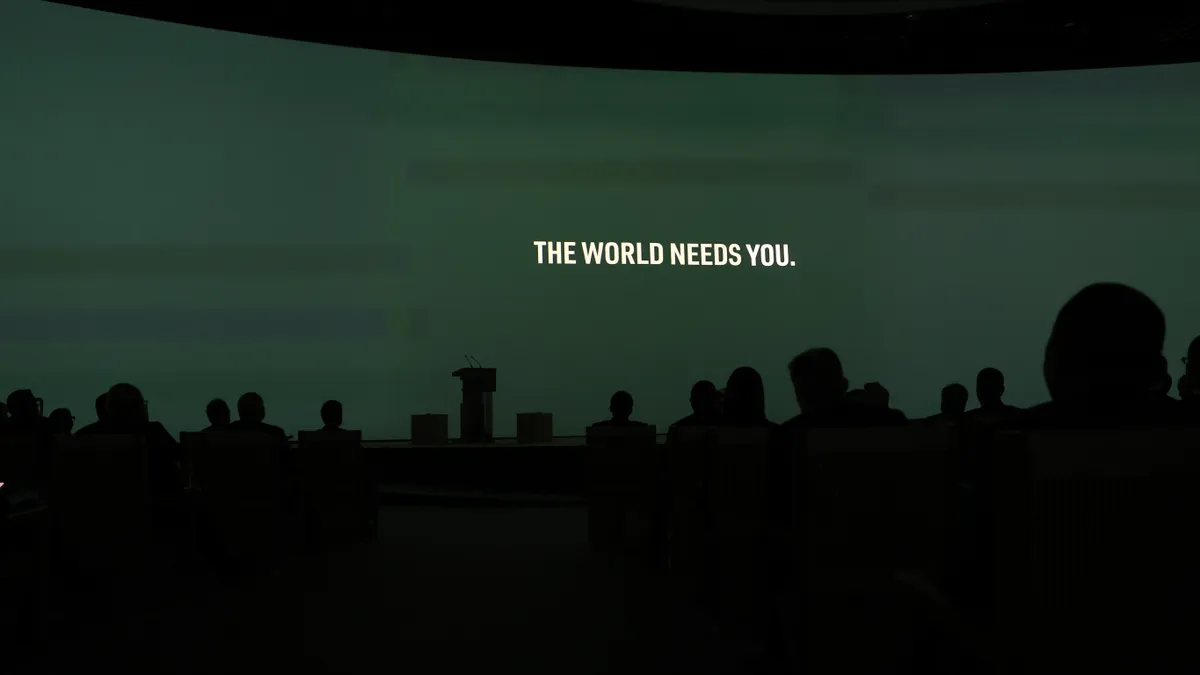 The words "The World Needs You" are projected on a screen.