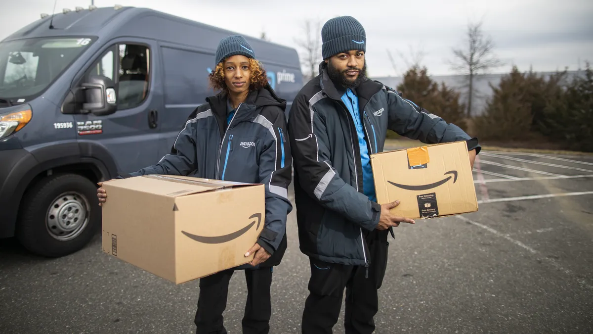 Two people wearing knit hats and company jackets holding packages.