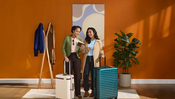 Two women standing in front of a wall with luggage by side