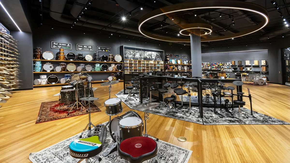 Drum kits and cymbals are displayed in a large open retail showroom