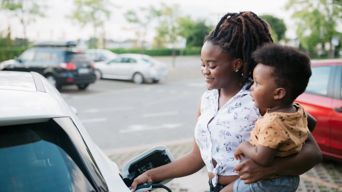 A woman charging her electric car and holding her baby.