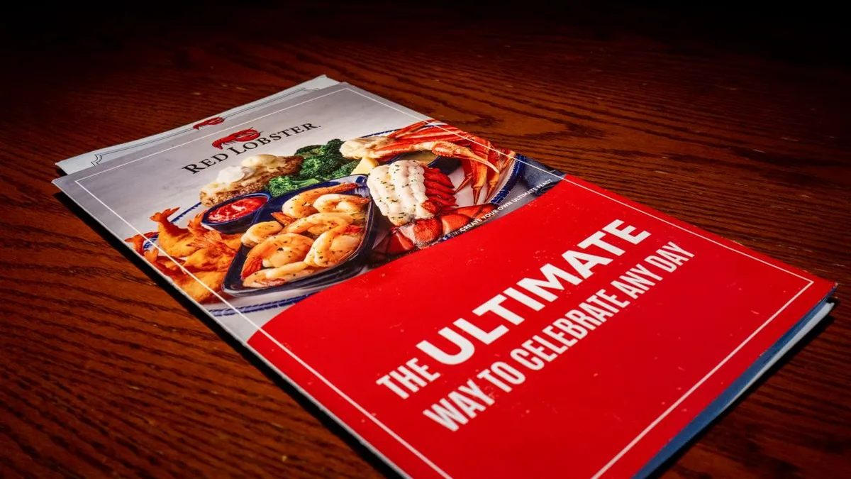 A menu with photos of shrimp, lobster tail with "The Utlimate Way to celebrate any day" underneath. The menu sits atop a dark table.